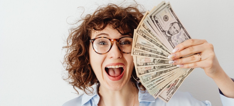 A woman holding a fan of dollar bills, happy not to have made some of the most common mistakes when installing solar panels.