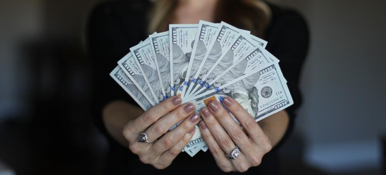 A woman holding dollar bills to pay for getting rid of pigeons on rooftops.