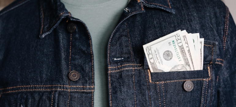 Dollar bills protruding from a denim jacket pocket.