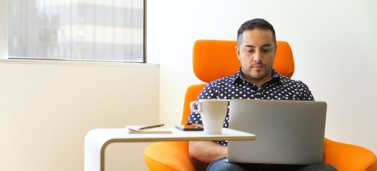 A man sitting in an orange sofa, using laptop to research different types of solar panels