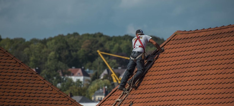 A worker in a safety harness taking care of some common causes of roof damage.