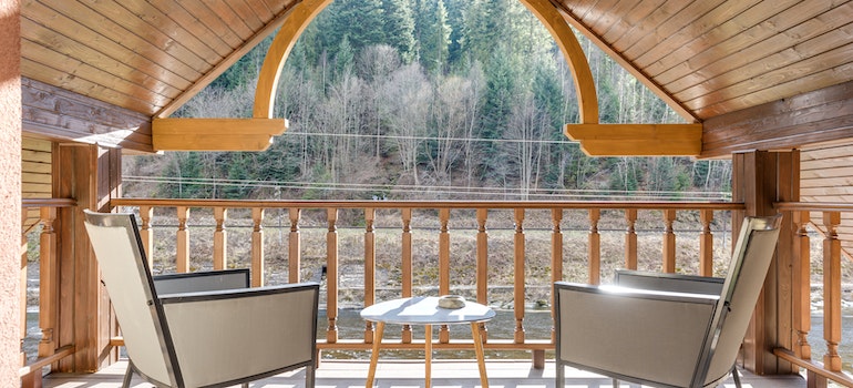 Attic and a patio of a house in the middle of the woods with two chairs and a small table